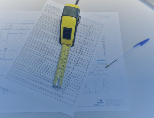 A yellow tape measure rests on top of several sheets of technical drawings and specifications. A blue pen is positioned nearby, suggesting a workspace focused on planning or construction.