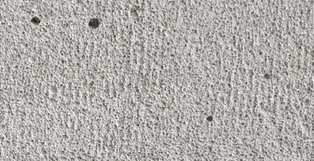 A textured surface with a light gray color, featuring small holes and a rough appearance. The pattern is consistent, creating a uniform look across the surface.