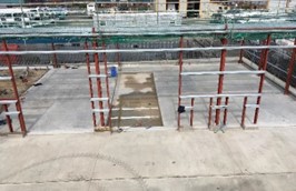 A construction site is visible, featuring a partially completed concrete floor and metal framework. Scaffolding and construction materials are present, indicating ongoing building work.