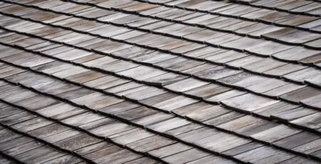 A close-up view of a wooden shingle roof, showcasing the textured and layered arrangement of the shingles. The varying shades of brown and gray create a natural, rustic appearance.