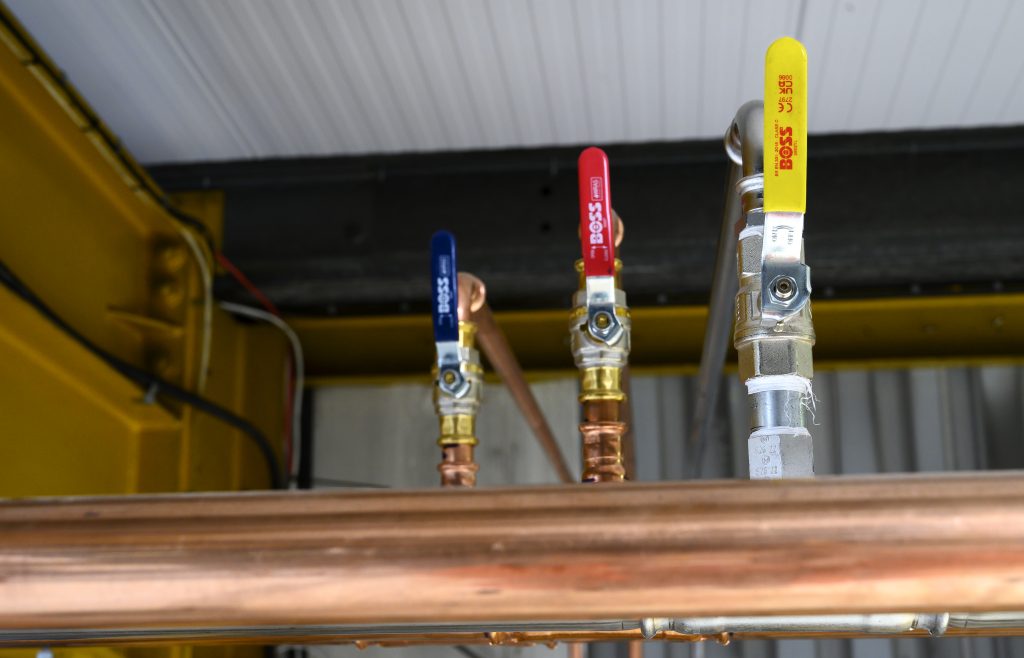 Three valves in different colors—blue, red, and yellow—are mounted on copper piping. The valves are part of a plumbing system, with visible connections and a metallic structure in the background.