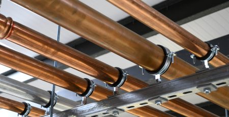 A network of copper pipes is mounted on a metal framework, showcasing their shiny surface and secure fittings. The pipes are arranged parallel to each other, with visible clamps holding them in place.