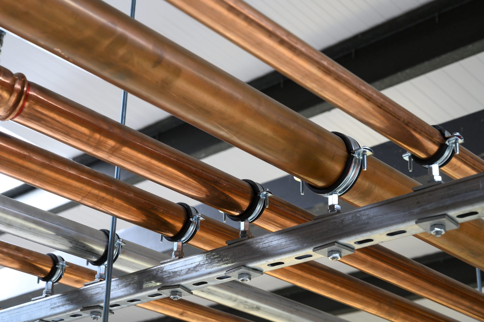 A network of copper pipes is mounted on a metal framework, showcasing their shiny surface and secure fittings. The pipes are arranged parallel to each other, with visible clamps holding them in place.